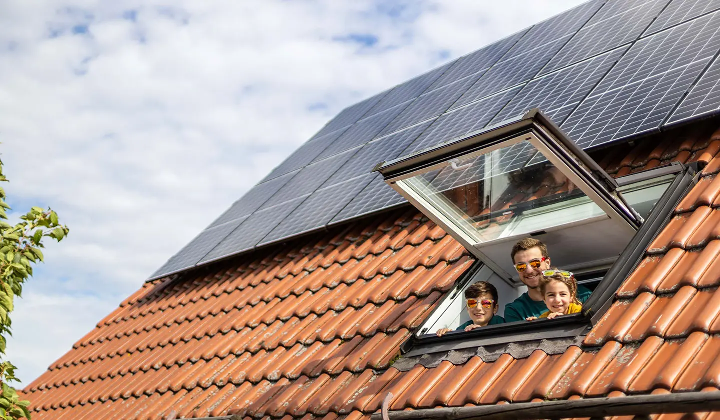 Eine Photovoltaikanlage auf einem Haus in Stuttgart. Die Familie schaut aus einem Dachfenster.