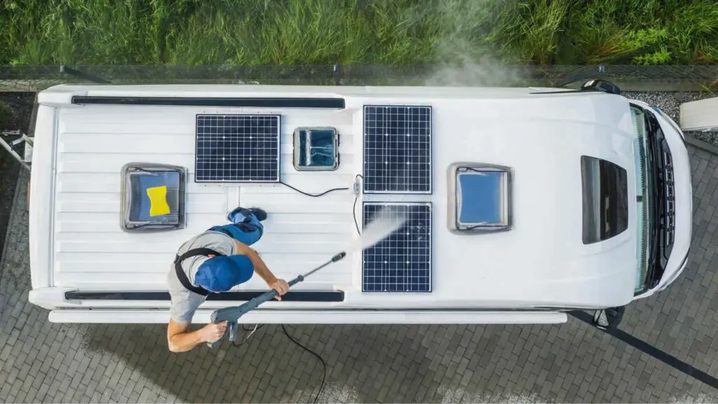 Ein Arbeiter reinigt 3 kleine Photovoltaikmodule auf dem Dach eines Wohnmobils.