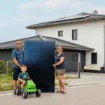 Familie steht vor einem Haus und hält ein Solarmodul in der Hand