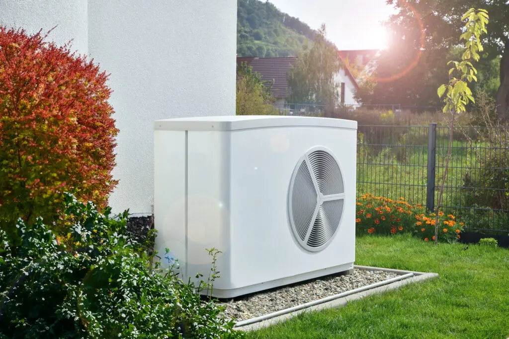 Eine Wärmepumpe steht in einem Garten vor einem Haus auf einem Kiesgrund.