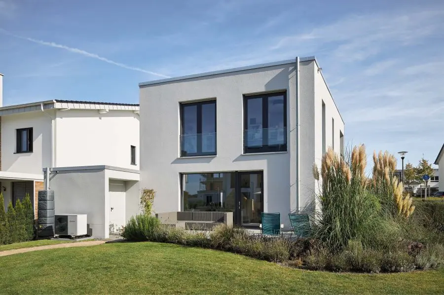 Ein Einfamilienhaus im Sommer mit einer Wärmepumpe neben dem Eingang