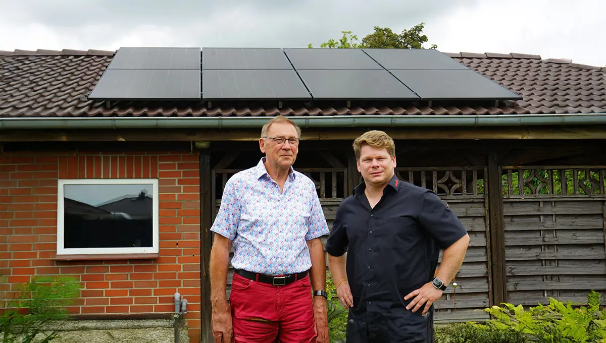 Herr Paegel und Björn Schumacher von enerix Rostock stehen vor einem Carport mit Solarmodulen auf dem Dach und blicken in die Kamera