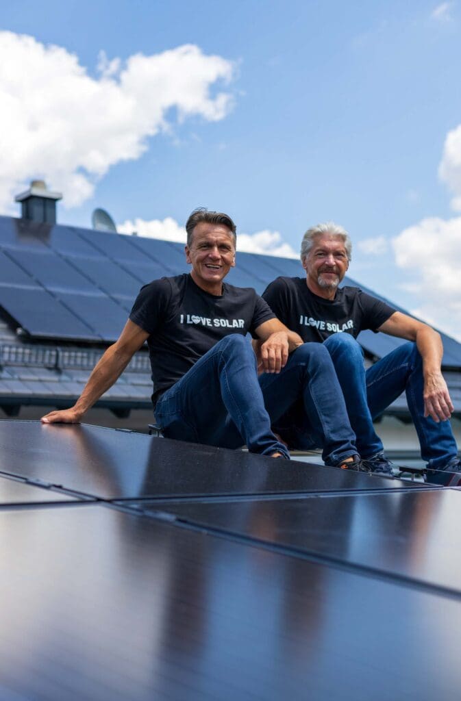 Die beiden Gründer von enerix Stefan Jakob und Peter Knuth sitzen auf einem Dach mit einer Photovoltaikanlage und lächeln in die Kamera.