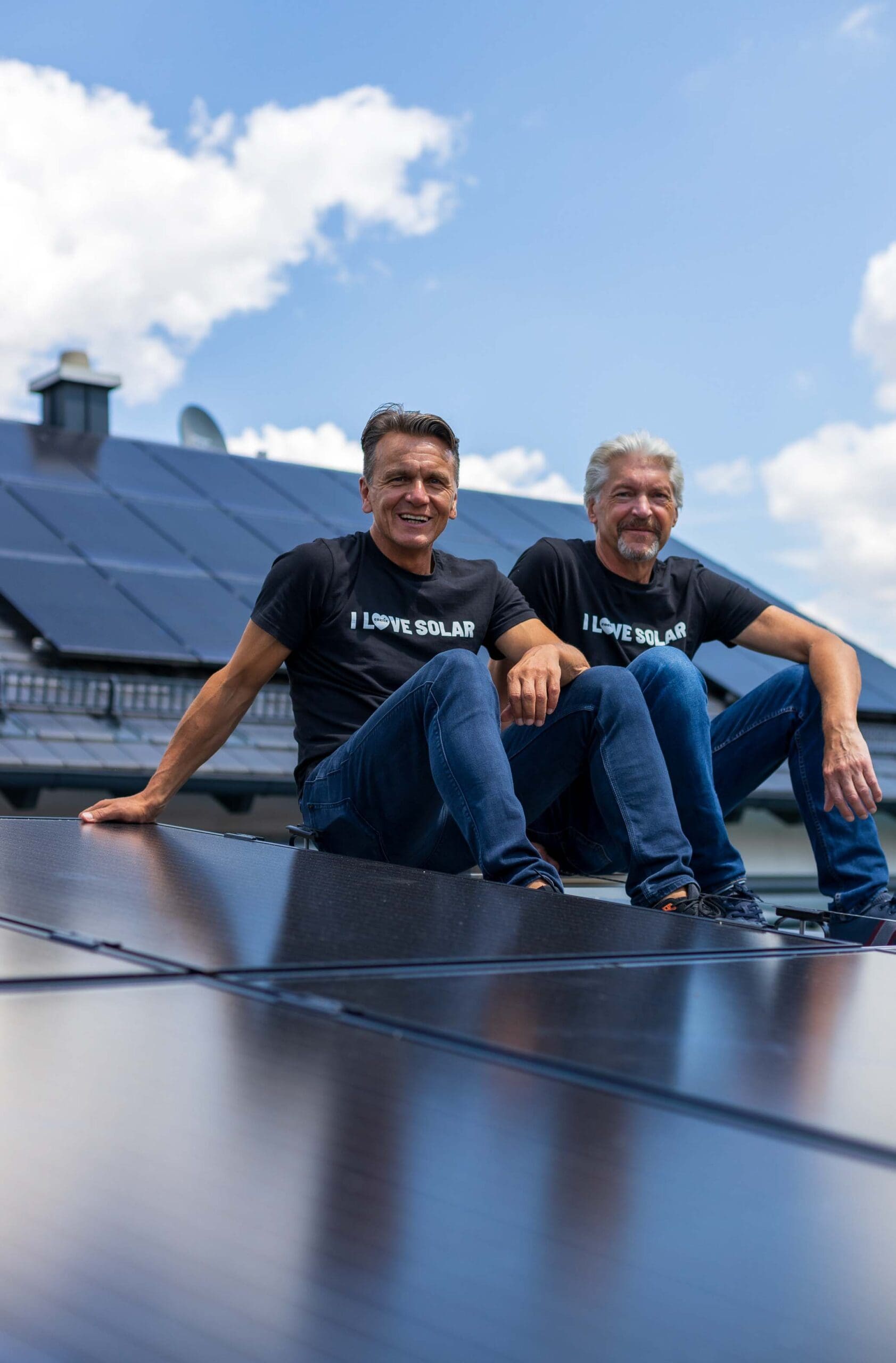 Die beiden Gründer von enerix Stefan Jakob und Peter Knuth sitzen auf einem Dach mit einer Photovoltaikanlage und lächeln in die Kamera.