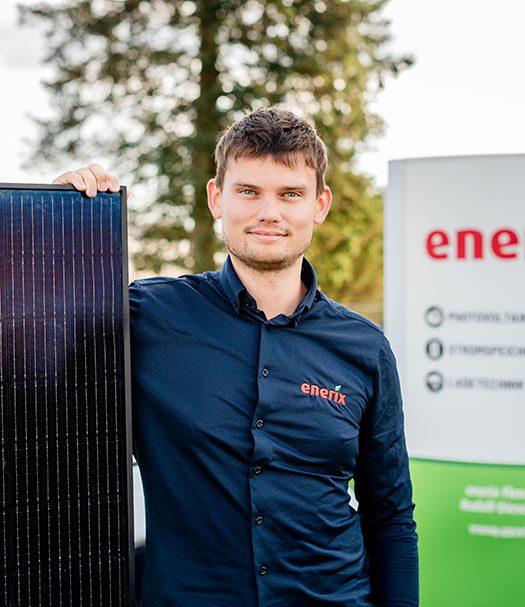 Ein enerix Mitarbeiter in einem dunkelblauen Hemd steht angelegt an ein Solarmodule vor einem enerix Schild.
