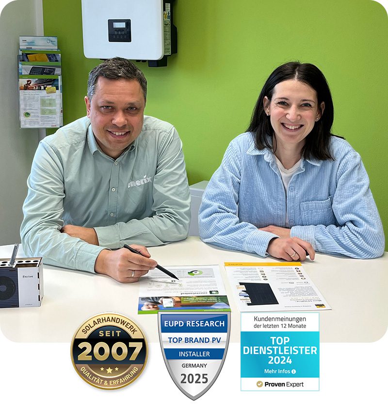 Zwei Mitarbeiter von enerix Cham sitzen in einem Tisch und lächeln in die Kamera. Vor Ihnen liegt ein Beratungsbogen für Photovoltaikanlagen