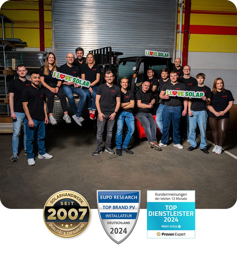 **Alt-Text:** Das Team von Enerix Paderborn posiert in einer Lagerhalle vor einem Gabelstapler. Die Mitarbeiter tragen schwarze Poloshirts mit dem Enerix-Logo. Einige sitzen auf den Gabeln des Staplers, während andere Schilder mit der Aufschrift „I Love SOLAR“ halten. Im Vordergrund sind drei Auszeichnungen zu sehen: „Solarhandwerk seit 2007“, „Top Brand PV Installateur Deutschland 2024“ und „Top Dienstleister 2024“.