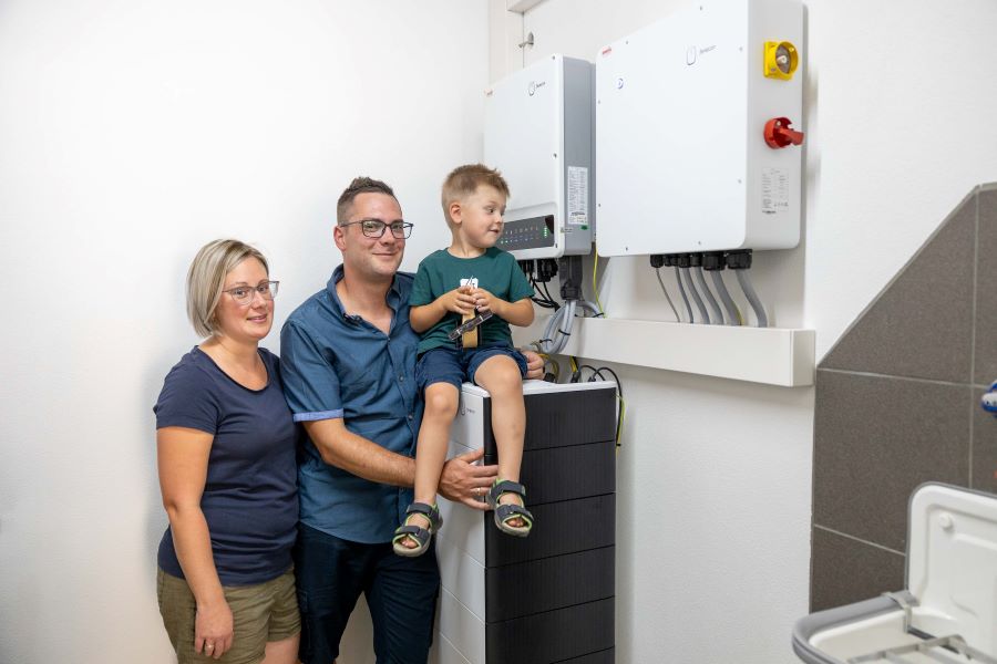 Eine Familie steht im Keller ihres Hauses vor ihrem Wechselrichter und hat den PV Speicher  
 nachgerüstet. 