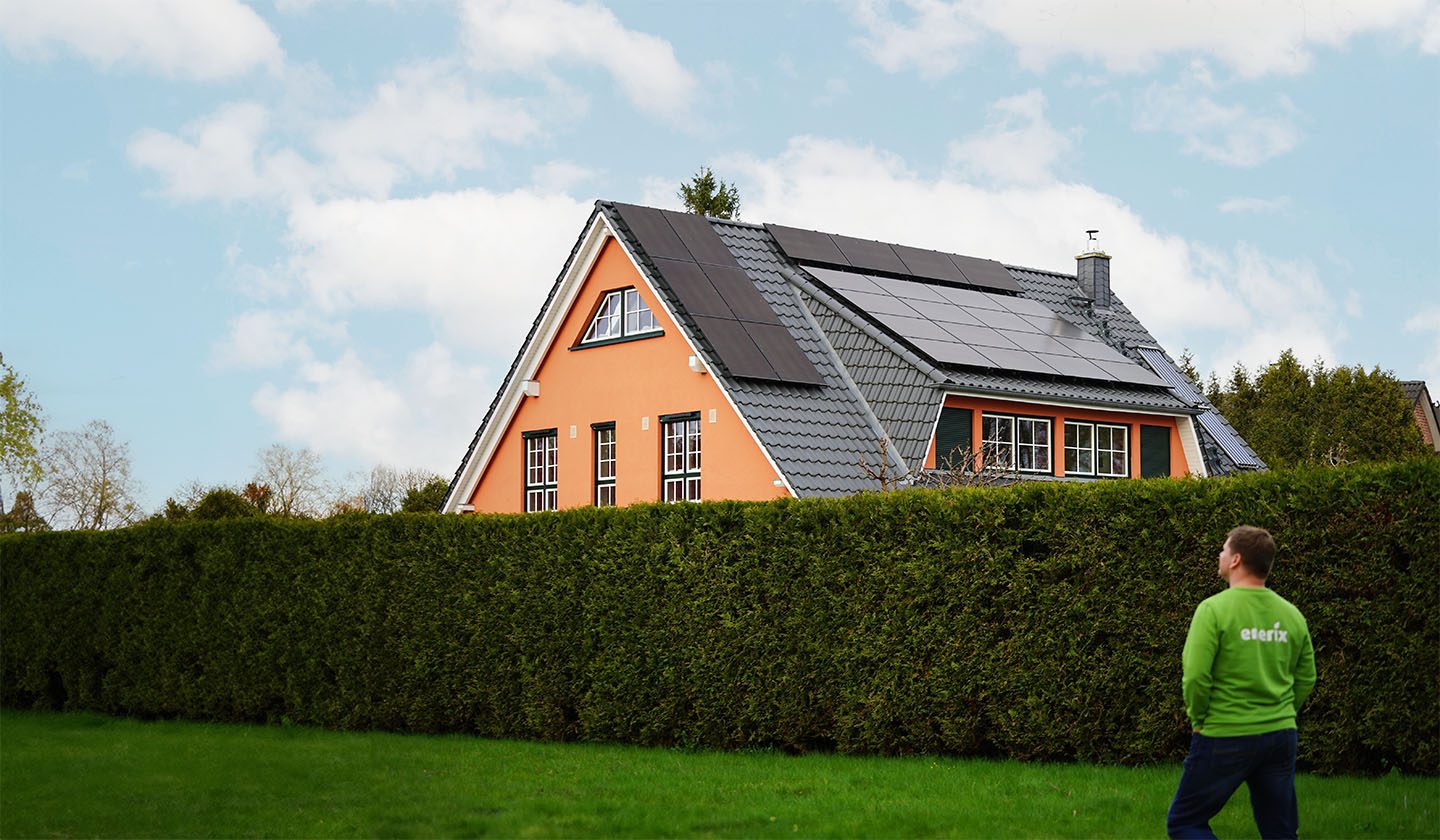 Der Geschäftsinhaber von enerix Rostock Björn Schuhmache steht vor einem Haus mit einer Photovoltaikanlage auf dem Dach und betrachtet diese.