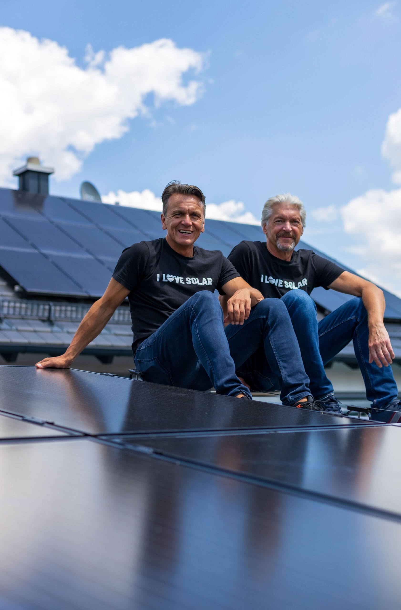 Die beiden Gründer von enerix Stefan Jakob und Peter Knuth sitzen auf einem Dach mit einer Photovoltaikanlage und lächeln in die Kamera.