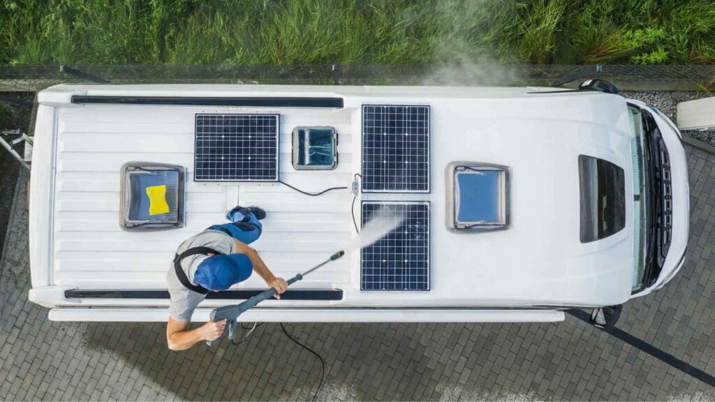 Ein Arbeiter reinigt 3 kleine Photovoltaikmodule auf dem Dach eines Wohnmobils.