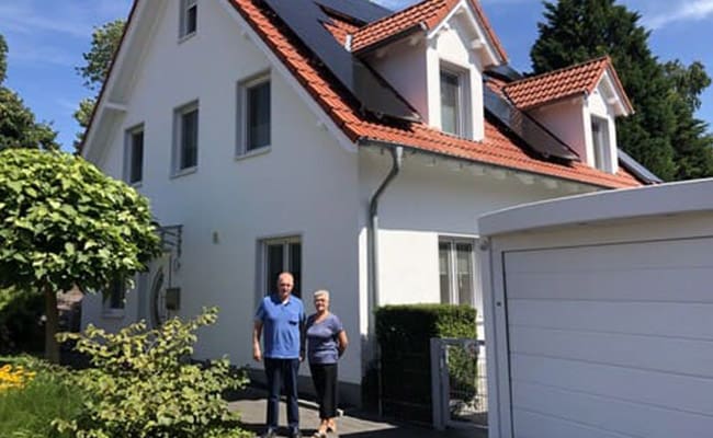 Ein Ehepaar steht vor ihrem Haus mit einer Photovoltaikanlage auf dem Dach.