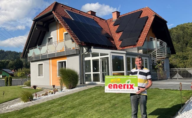 Eine Photovoltaikanlage auf einem Hausdach, der Eigentümer steht davor im Garten und hält ein enerix Schild in der Hand.