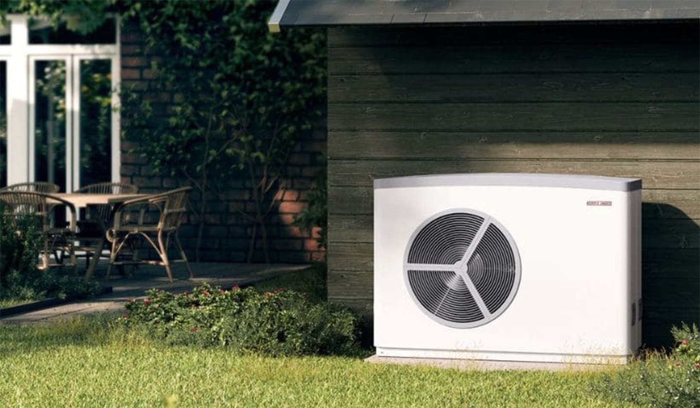 Eine Wärmepumpe steht im Garten von einem Einfamilienhaus.