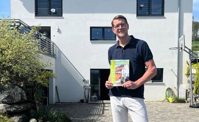 Ein zufriedener Kunde von enerix vor seinem Haus hält einen enerix-Leitfaden in der Hand.