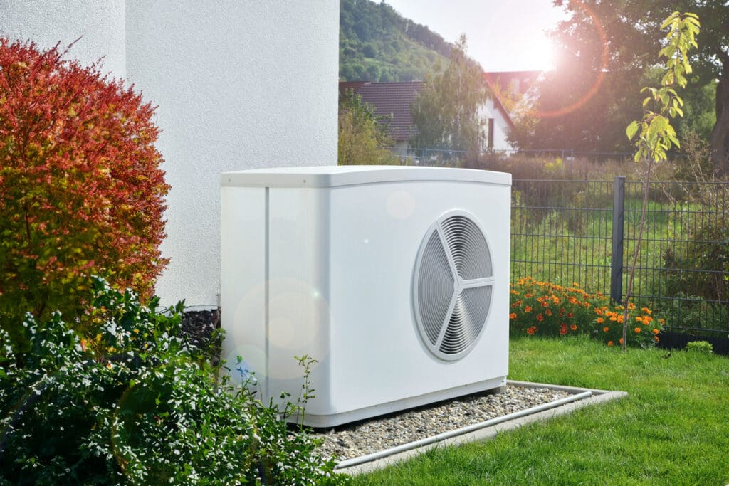Eine Wärmepumpe steht in einem Garten vor einem Haus auf einem Kiesgrund.