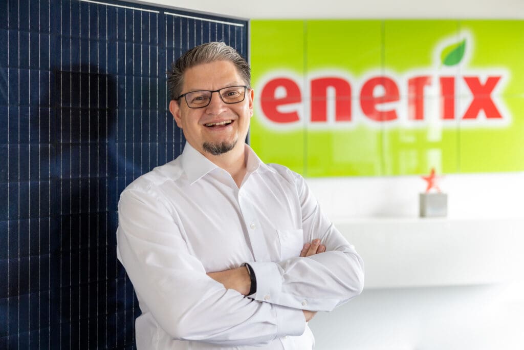 Der Geschäftsinhaber von enerix Elbe-Havelland Marko Schollbach steht vor einem Photovoltaikmodul und enerix Logo im Hintergrund.
