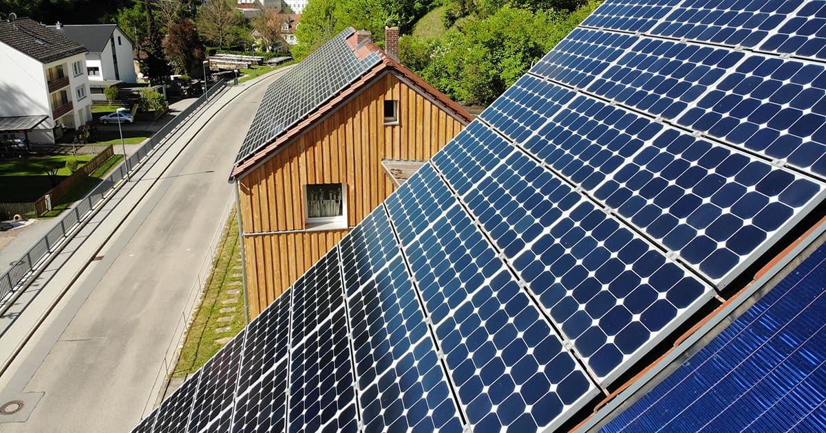 Zwei Holzhäuser mit jeweils einer großen Photovoltaikanlage auf dem Dach.