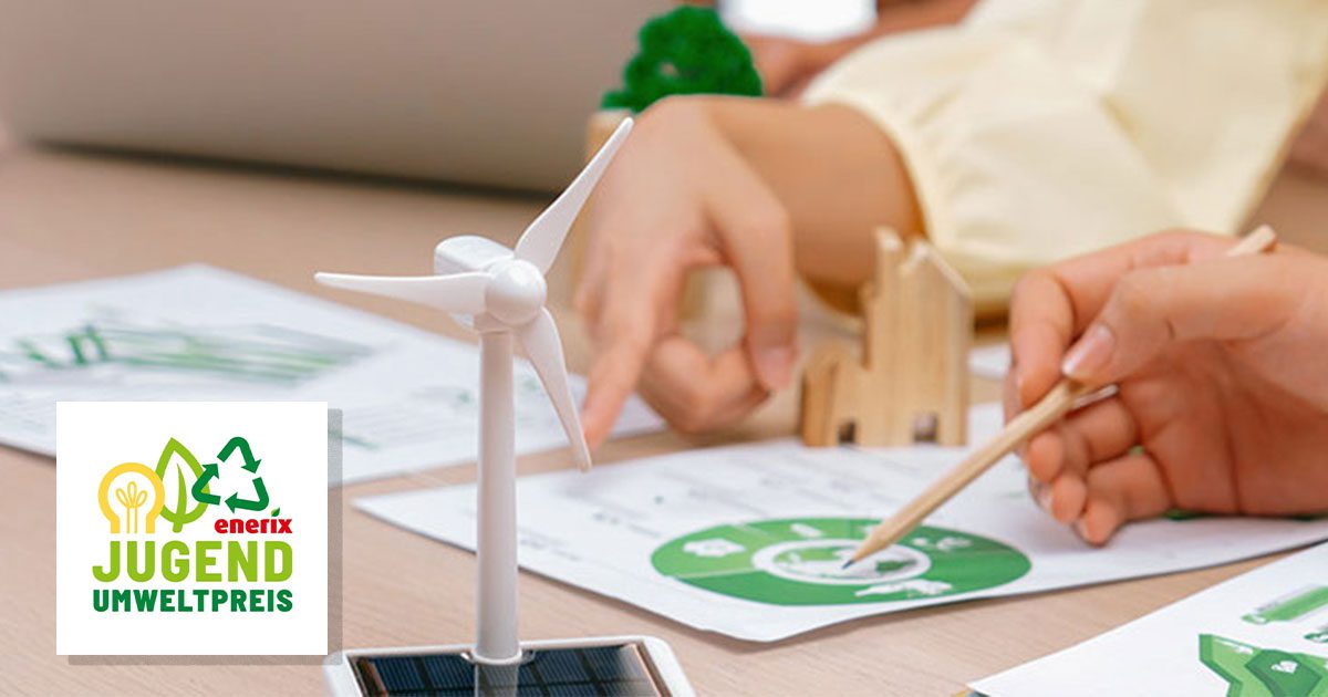 Zwei Personen lesen ein Informationsblatt an einem Tisch. Im Vordergrund ist ein kleines Windradmodell zu sehen.