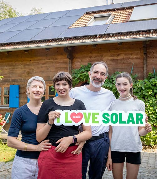 Eine 4-köpfige Familie steht vor ihrem Haus mit Photovoltaikanlage und hält ein "I LOVE SOLAR"-Schild in der Hand.