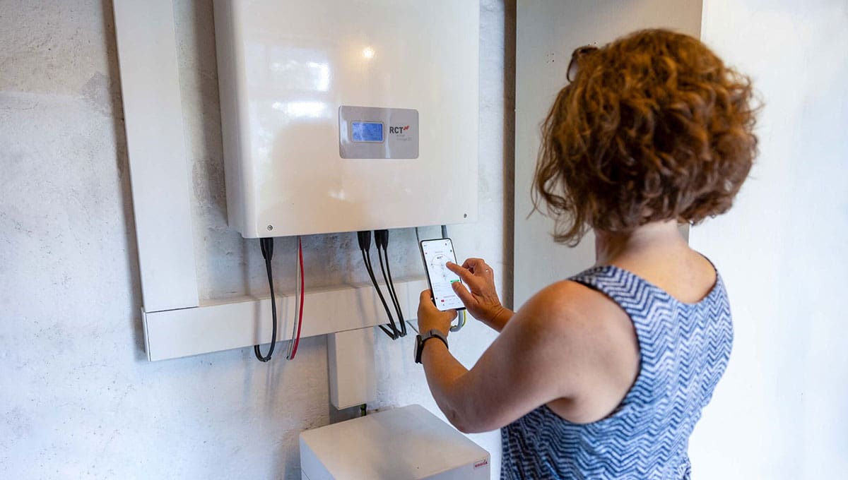 Eine Frau hat ein Handy in der Hand uns steht vor einem Wechselrichter.