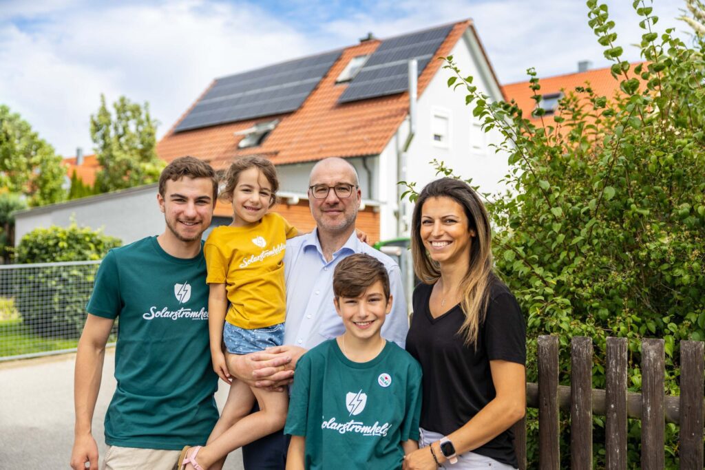 Eine fünfköpfige Familie steht vor ihrem Haus mit einer neu montierten Photovoltaikanlage und freut sich über das Ergebnis.