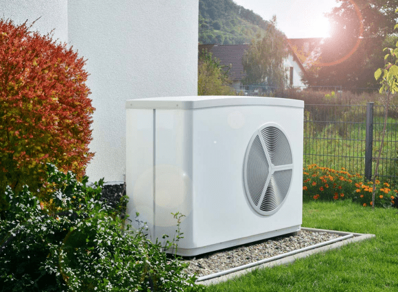 Eine Wärmepumpe in einem Garten vor einem Haus auf einem Kiesgrund.
