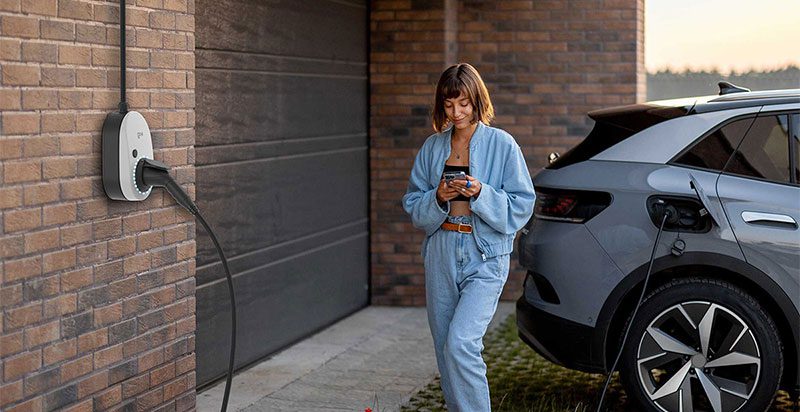 Eine junge Frau die vor einem E-Auto steht. Das E-Auto wird über eine Wallbox von go-e geladen