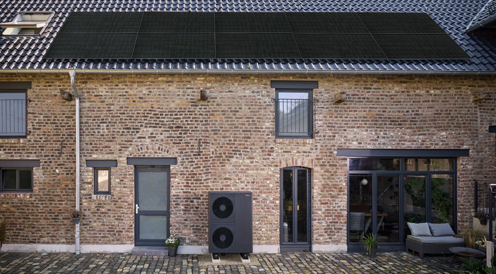 Ein Haus aus Backstein mit einer PV Anlage auf dem Dach und einer Wärmepumpe neben der Tür. 