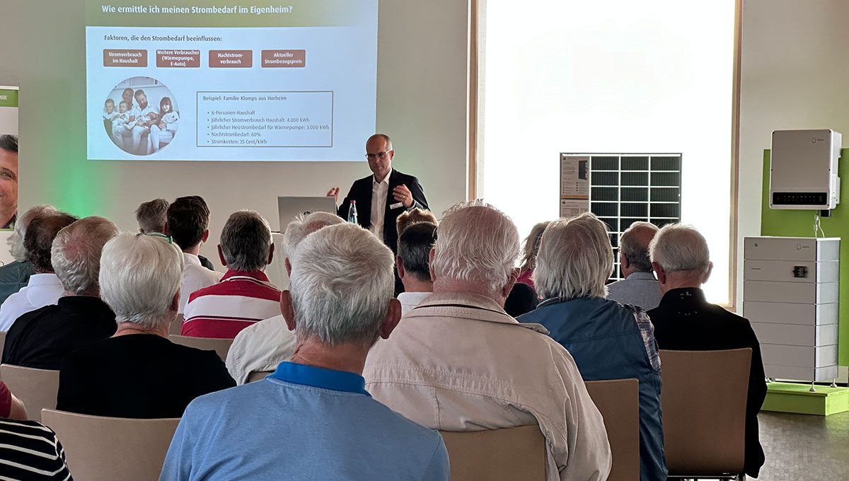 Der Geschäftsinhaber von enerix Südschwarzwald hält einen Vortrag bei einem Infoabend zum Thema Photovoltaik mit vielen Gästen. Im Hintergrund ist eine Leinwand und verschiedene Ausstellungsprodukte.