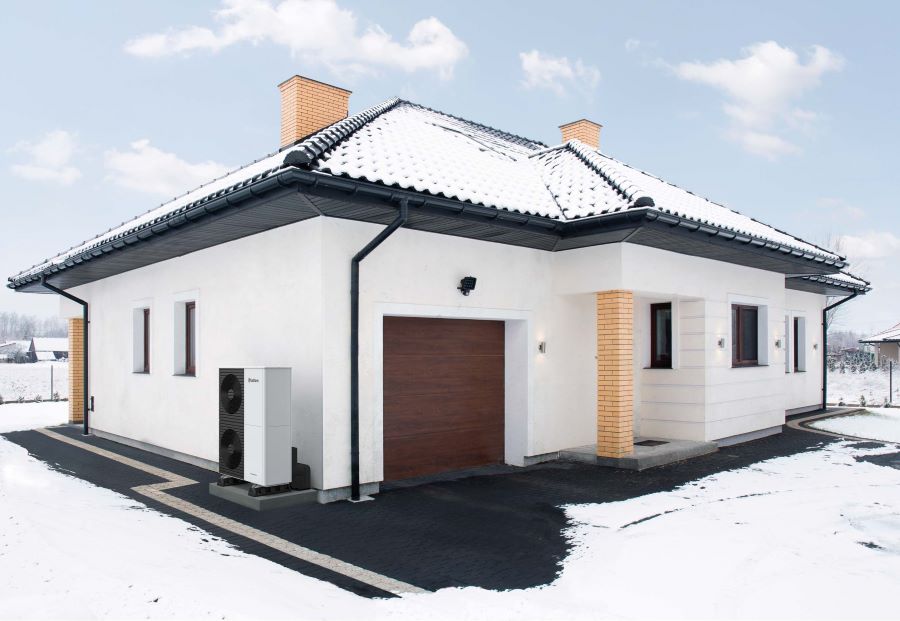 Waermepumpe vor einem Einfamilienhaus im Winter.