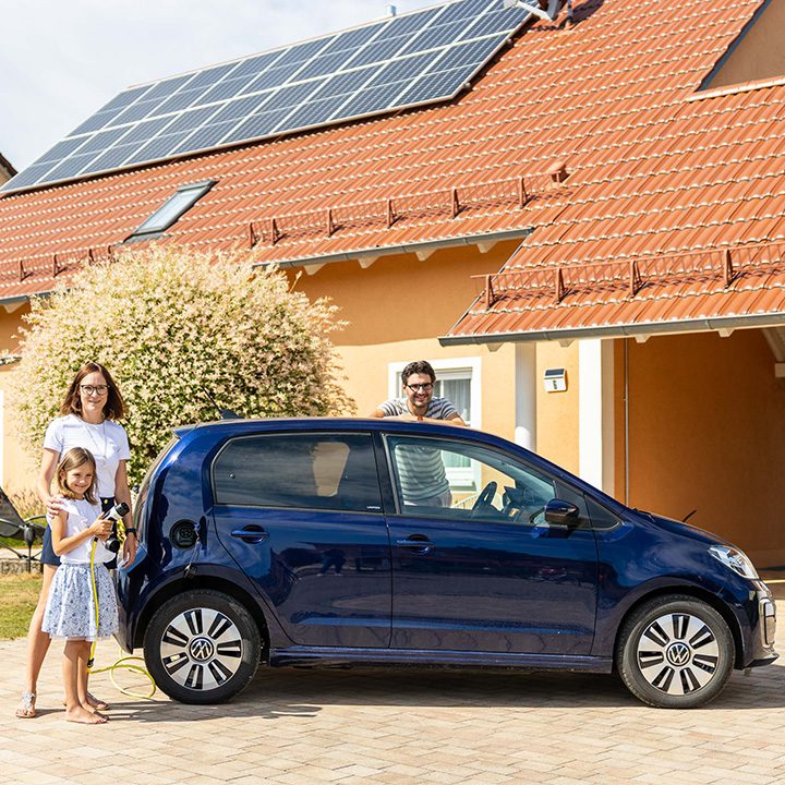 Eine Familie steht vor einem Haus mit Photovoltaikanlage auf dem Dach und einem Elektroauto