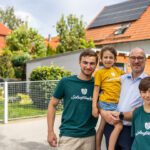 Eine Familie steht glücklich vor einem Haus mit einer Photovoltaikanlage auf dem Dach
