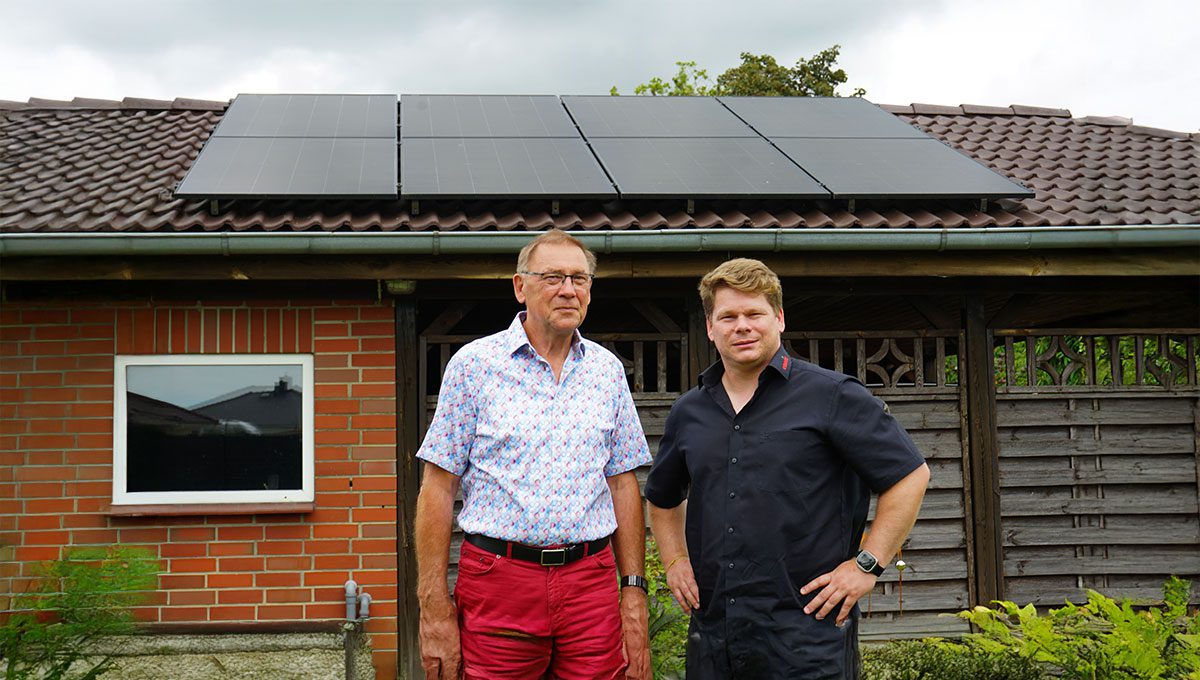 Herr Paegel und Björn Schumacher von enerix Rostock stehen vor einem Carport mit Solarmodulen auf dem Dach und blicken in die Kamera