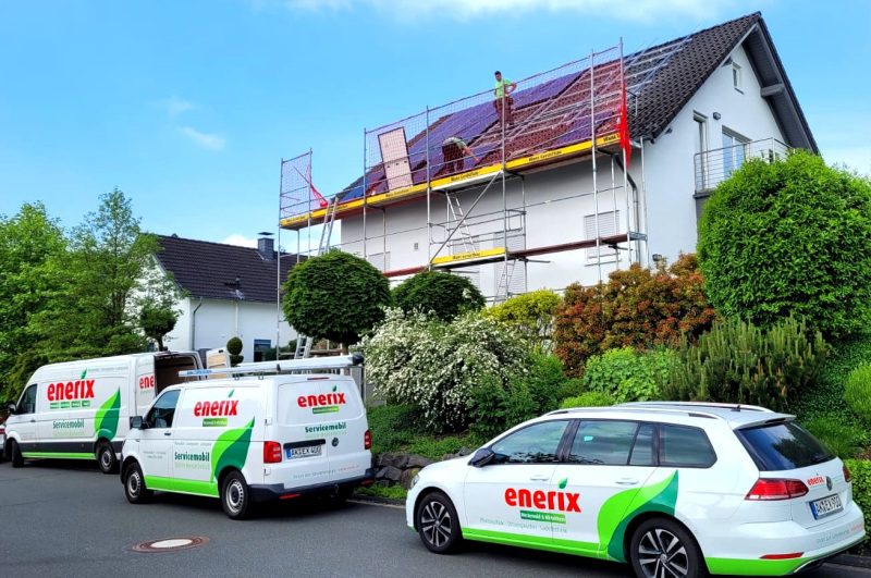 Photovoltaik Montagepartner von enerix installieren eine Solaranlage auf einem Hausdach. Vor dem Haus stehen enerix Fahrzeuge