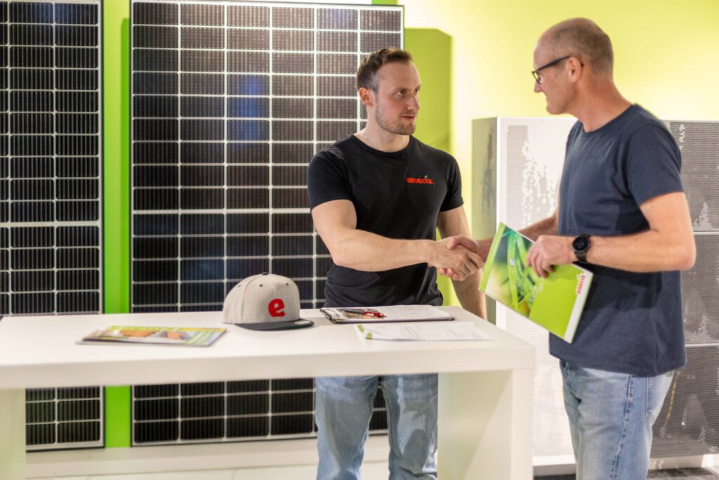 Ein enerix Fachberater schüttelt einem Kunden freundlich die Hand. Im Hintergrund sind Solarmodule zu sehen.