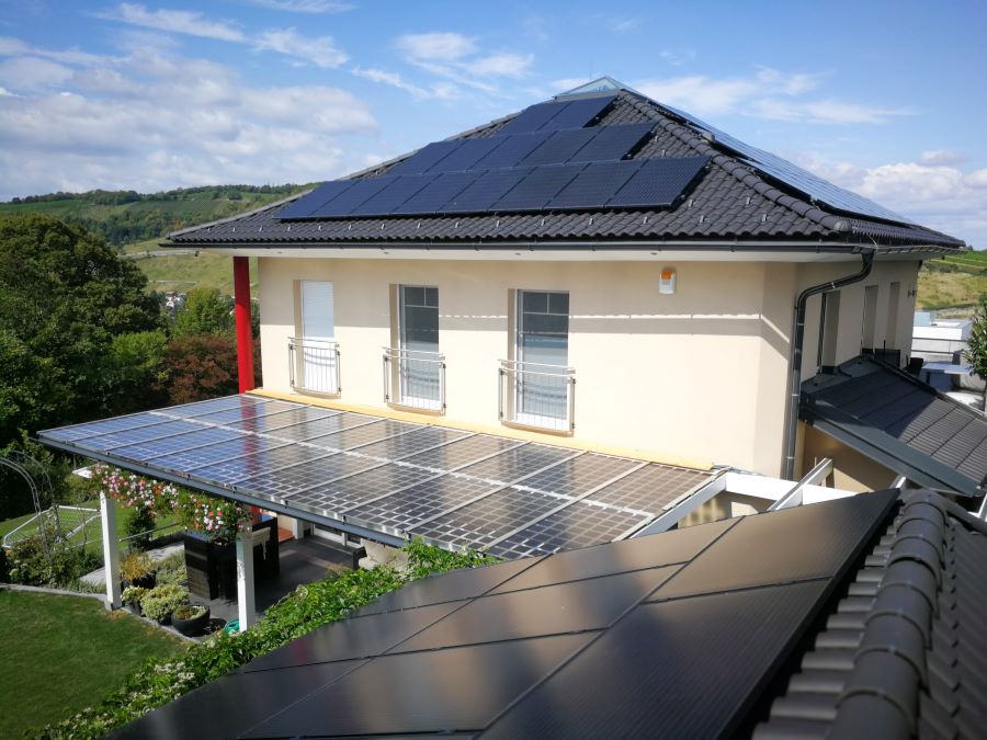 Einfamilienhaus mit Photovoltaikanlage auf dem Dach, die von Sonne angescheint wird.
