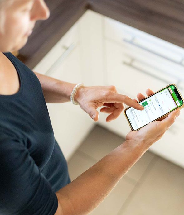 Eine Frau steht in einer Küche und bedient das Energiemanagementsystem enerixControl auf ihrem Smartphone