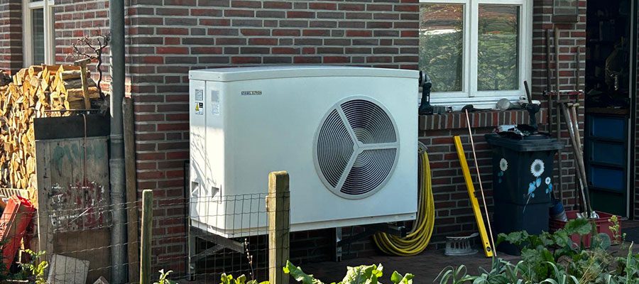 Außeneinheit einer Luft-Wasser-Wärmepumpe auf einem Ziegelfliesen-Untergrund, montiert an der Außenwand eines Einfamilienhauses – enerix Weser-Ems.