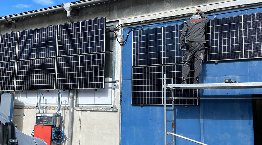 Ein enerix Monteur installiert Solarmodule an einem großen Garagentor einer KFZ Werkstatt