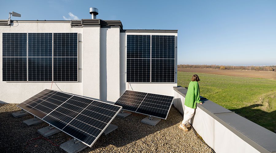 Frau blickt über Feld neben Haus mit kombinierten Photovoltaikanlagen an Fassade und Flachdach – Beispiel für wirtschaftliche Nutzung von Fassaden-PV.