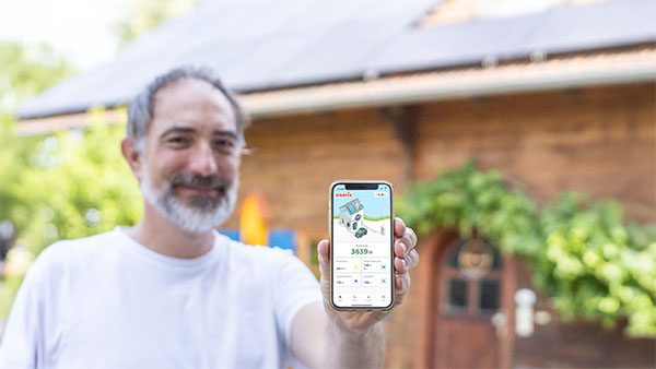 Ein Mann steht vor seiner Photovoltaikanlage und hält sein Handy mit der App enerix Control in die Kamera.
