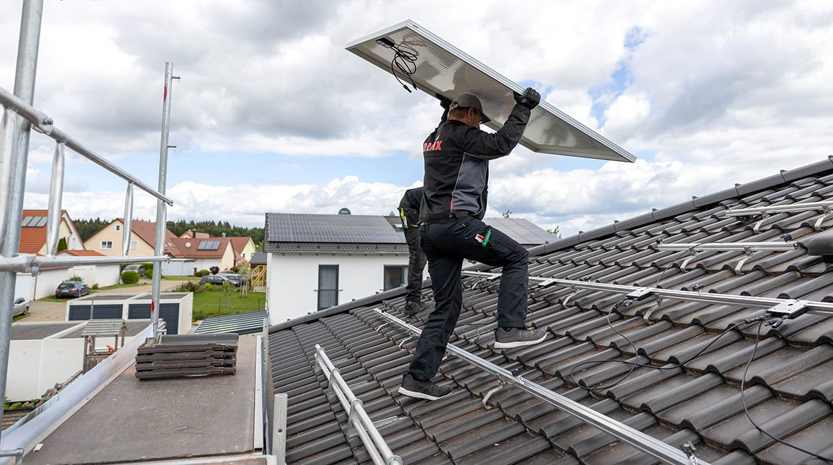 Handwerker verschraubt ein Photovoltaikmodul auf dem Dach, Montage mit Unterkonstruktion sichtbar.