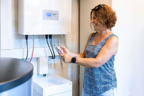Eine Frau steht mit einem Handy vor dem nachgerüsteten PV Speicher und freut sich über die Einsparung.
