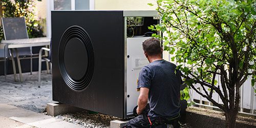 Eine enerix-Mitarbeiter installiert eine Wärmepumpe im Außenbereich eines Hauses