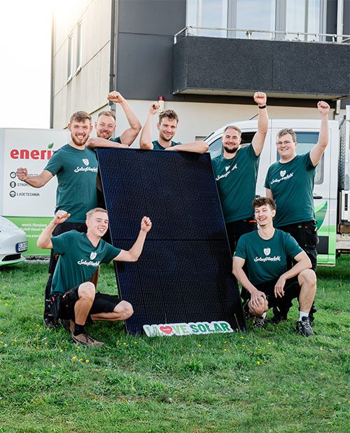 Foto vom Photovoltaik Montageteam das vor einem großen Solarmodul steht.