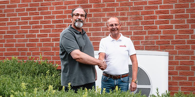 Ein freundlicher enerix Fachberater schüttelt einem zufriedenen Kunden die Hand, im Hintergrund ist eine weiße Wärmepumpe zusehen.