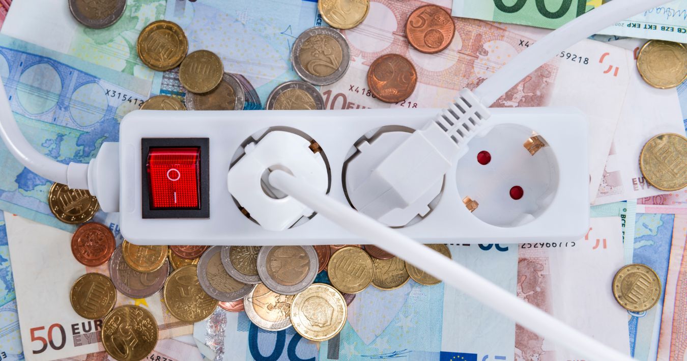 Mehrfachsteckdose mit eingeschaltetem Schalter liegt auf Euro-Scheinen und -Münzen – Symbolbild für Stromkosten und Energieverbrauch