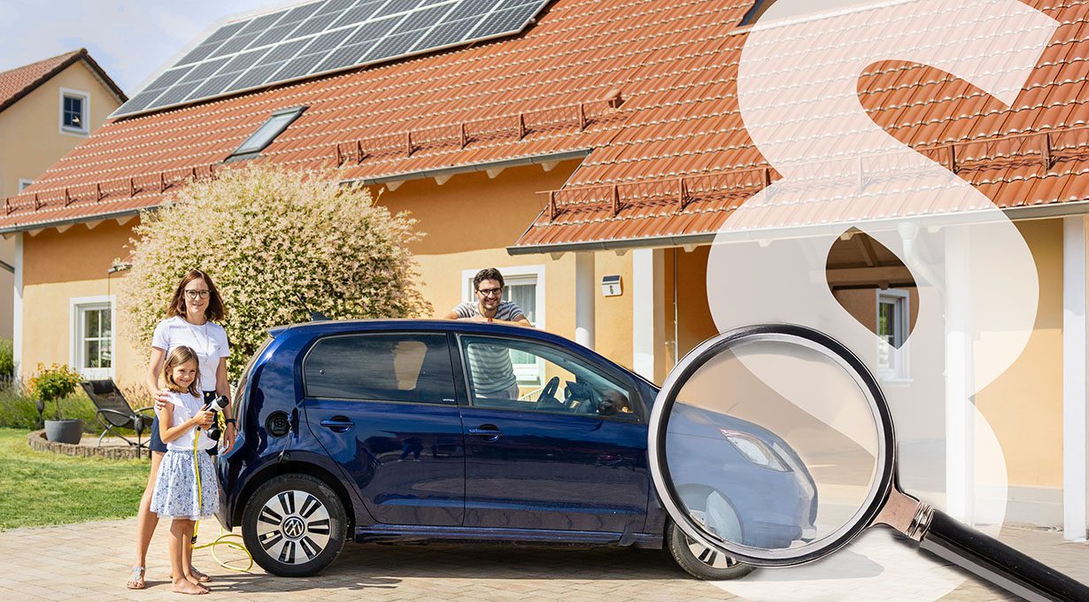 Familie vor Einfamilienhaus mit Photovoltaikanlage auf dem Dach: Mutter und Tochter stehen barfuß in der Einfahrt und laden ein blaues Elektroauto, im Hintergrund lehnt der Vater an der Motorhaube; darübergelegt ein großes Paragrafenzeichen und eine Lupe als Symbol für gesetzliche Regelungen.