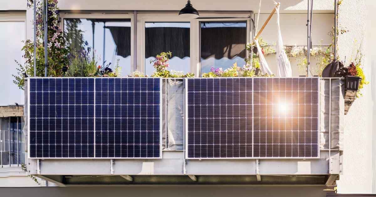 Zwei Solarpanels auf einem Balkon, umgeben von Pflanzen, mit Sonnenlicht, das auf die Solarmodule scheint.